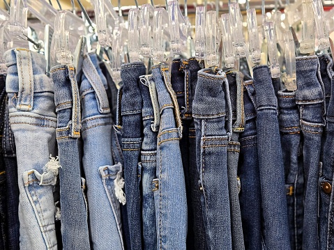 Distressed blue jeans hanging on hangars in a clothing rack in a boutique