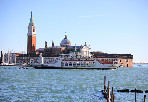 church and high bell tower of Saint George in Giudecca canal in Venice with boats and ferryboat in Italy