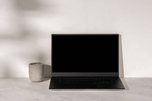 istock Open laptop computer with empty black screen, candle on marble neutral taupe table, textured plaster wall background with natural abstract sunlight shadows 2089399955