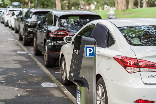 Sydney, NSW, Australia, February 20th 2024. A parking meter is in focus, and a row of cars is parked along a sidewalk in the background.