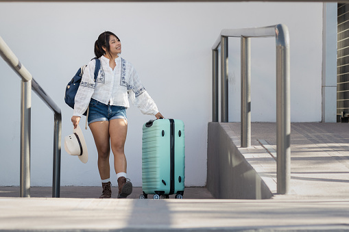 Horizontal photograph with copy space of a pretty young 26 year old woman traveling alone, excited to explore Mexico; She arrives at the bus station with her suitcase and backpack