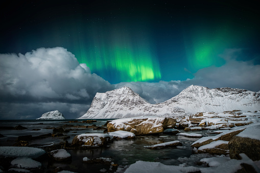 Beautiful northern lights over snow covered mountain peaks at the arctic coastline of the Lofoten Islands in Nordland, Norway