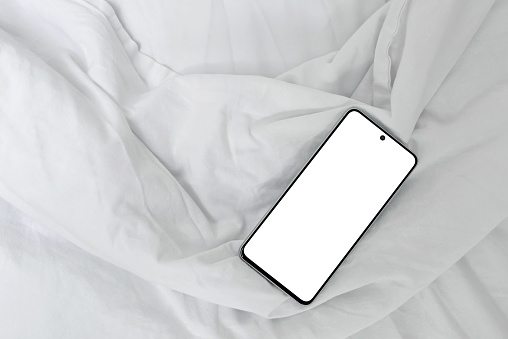 Mobile phone with blank screen mockup on bed with white crumpled cotton sheet and blanket background, lifestyle home interior, minimal business branding template.