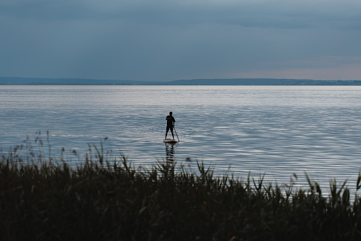 young man standing on sup and paddling on water of calm lake, tranquil scenery. High quality picture