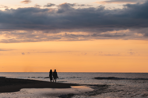 romantic couple of man and woman walking on sand beach at beautiful sunset. High quality picture