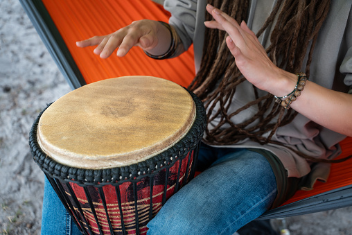 person with dreadlocks play tribal reggae at small African hand drum djembe. High quality picture