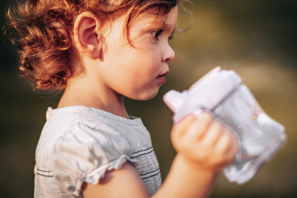 Cute, little curly girl drinks water from her plastic bottle