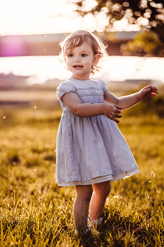 Cute, little girl in white dress looking at something. Afternoon light