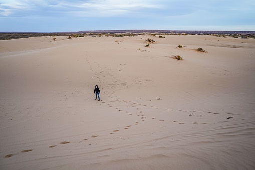 A male teenager stands at the bottom of a Sand Dune in the Chihuahua Desert at Lincoln National Forest, a national park covering 1.1 million acres and three mountain ranges in southeastern New Mexico administered by the US Forest Service.