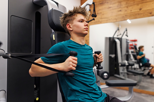 Teenage boy training in gym. He is build arm and chest muscles at the gym\nShot with Canon R5