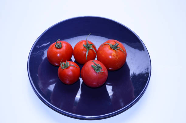 ripe, red tomatoes on a blue plate on a white background. A tasty and healthy vegetable rich in vitamins and minerals. dietary fruit or salad ingredient. isolated. view from above