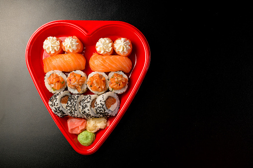 Black smooth table with a glamorous red heart-shaped plate and set of sushi with red sea fish and white rice