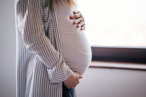 Photo of pregnant woman standing and holding hands on her belly.