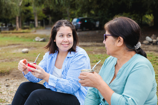 Generational Tradition: Latin Mother and Adult Daughter Share Yerba Mate on Blanket in Countryside Landscape