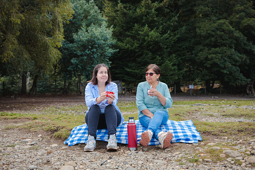 Latin Mother and Adult Daughter Bonding and Sharing Yerba Mate Outdoors sitting on a blanket in Natural Patagonian Space