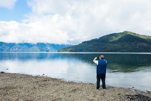 Patagonian Tranquility: Latin Middle-aged Man Enjoying Nature taking a photo with Mobile by Mountain Lake. Copy space