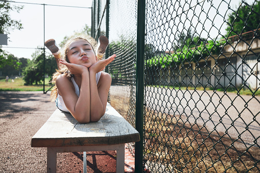 Funny portrait of a teenage girl making faces while lying on a bench on a sports field.