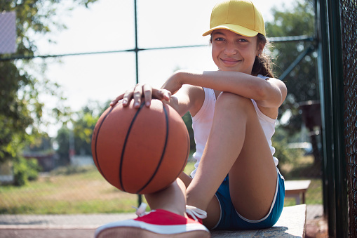 Portrait of a beautiful smiling teenage girl with basketball - ball in sports court.