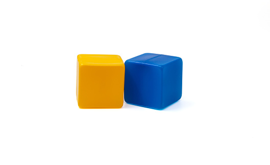 Multicoloured plastic cubes for children's games. Yellow and blue cubes lying side by side. White background. One near the other. Horizontal. High quality photo.