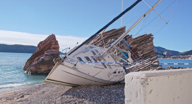 Broken yacht lies on beach near rock, fenced off with barrier tape. Crash site