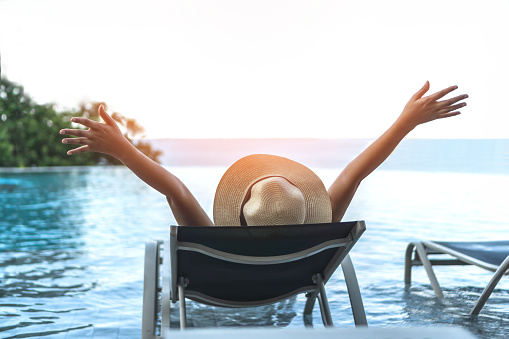 Holiday relaxation vacation of woman take it easy, happy life quality, resting on beach chair at swimming pool poolside beachfront resort hotel with summer sea sky ocean view background