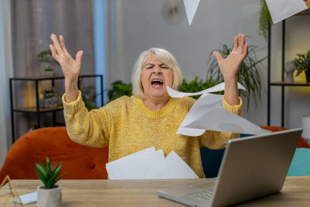 stressed senior woman looking at unpaid bank debt loan doing paperwork planning budget throws bills - pleading women business sadness photos et images de collection