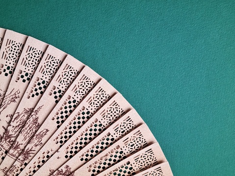 Open perforated bamboo fan with a pattern on a green background