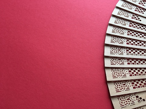Open perforated bamboo fan with a pattern on a red background. Space for text