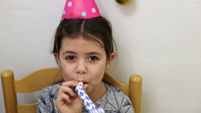 A little girl blows a whistle on a birthday party.