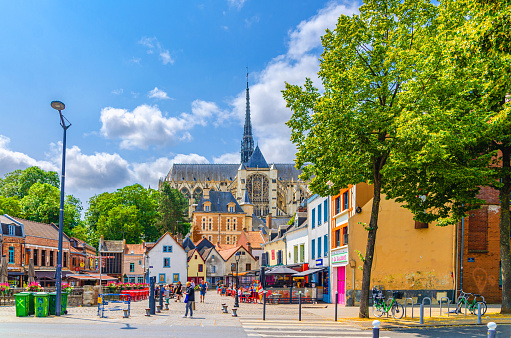 Amiens, France, July 3, 2023: old town Saint-Leu quarter Place du Don square with multicolored houses, walking tourists people and Cathedral Basilica of Our Lady of Amiens Roman Catholic church