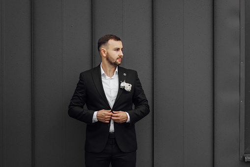 stylish and elegant groom in a black suit and white shirt on a dark background