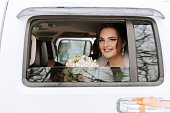 A beautiful bride with a bouquet of flowers is looking at the camera while sitting in a stylish white car.