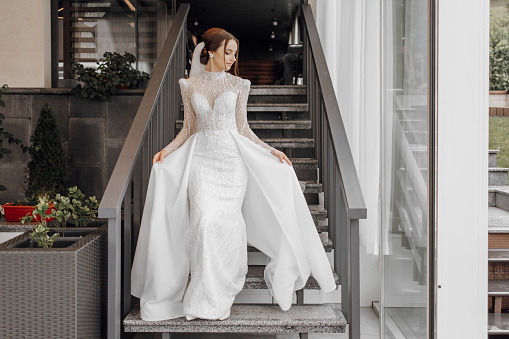 a full-length bride in a fashionable wedding dress on the steps of a restaurant walks forward and shows off her dress. Wedding day. The best event