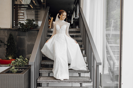 a full-length bride in a fashionable wedding dress on the steps of a restaurant walks forward and shows off her dress. Wedding day. The best event
