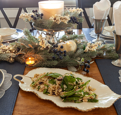 Leaf shaped China plate holding Feta cheese, spinach, and orzo and a silver spoon on a formal dining table.