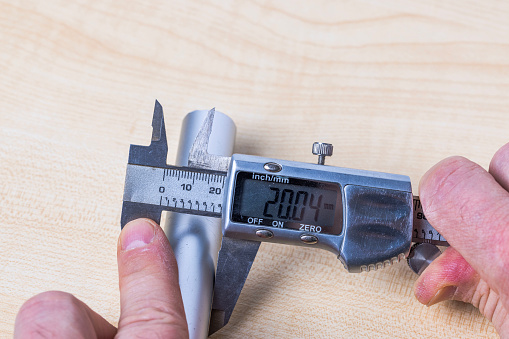 Close-up view of a person measuring the diameter of an aluminum pipe with a digital caliper.