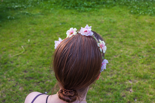 Close-up view of a young girl adorned with a hair decoration, gazing at the lush green grass lawn. Sweden.