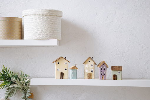 Five wooden miniature houses, each unique in design and color, on a white shelf against a textured white wall. Concept for home decor, mortgage, purchase, rent, real estate insurance.