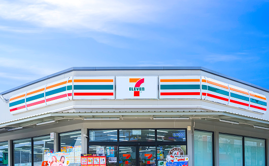 Samut Sakhon, Thailand - March 11, 2024 : Front view of modern 7 Eleven Convenience Store Building with geometric polygonal flat slab roof against blue sky background