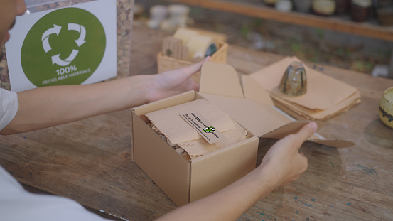 Close up of SME business owner chooses to use eco-friendly packaging, utilizing recyclable cardboard and water hyacinth cushioning for their pottery, showcasing an environmentally conscious and waste reduction approach