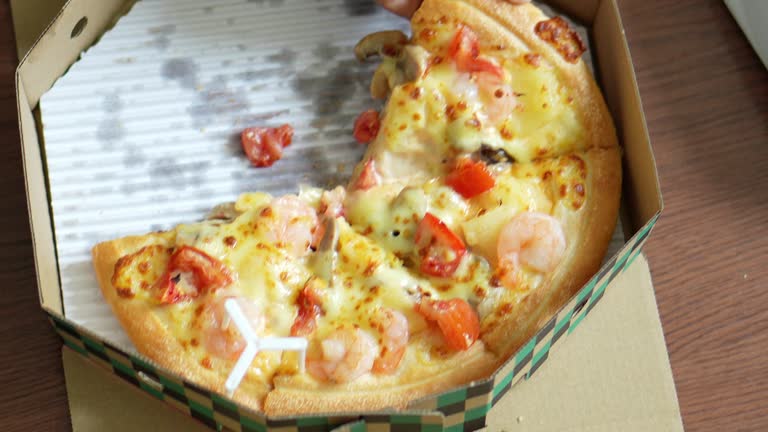 Boy is holding a slice of pizza is cut in half and is placed in a cardboard box.