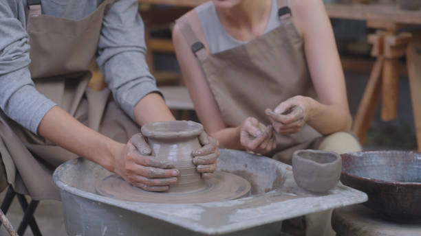 Potter's Hands Crafting on the Wheel Hands of a potter masterfully shape clay on a spinning potter's wheel, creating a new piece in a pottery studio filled with earthenware. Southeast Asian and Thai ethnicity model, Males and Females, including white people, 25-29 years homemade pottery wheel stock pictures, royalty-free photos & images