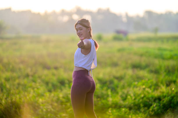 An Asian beauty woman stands beside a padi field at a villa on Bali island, her hand forming a heart shape, with the sunrise casting rays over lush rice paddies. Looking at camera.