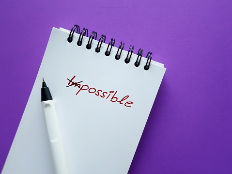 Pencil and notebook on purple background with text written IMPOSSIBLE crossed of to POSSIBLE, concept of  keeping in mind to make the impossible possible, focus on all the ways to accomplish your goals and make it happen