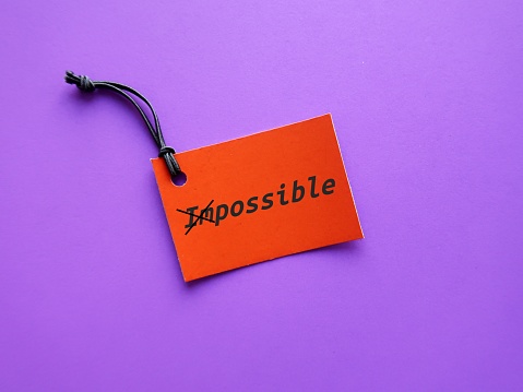 Orange paper tag on purple background with text IMPOSSIBLE crossed of to POSSIBLE, concept of  keeping in mind to make the impossible possible, focus on all the ways to accomplish your goals and make it happen