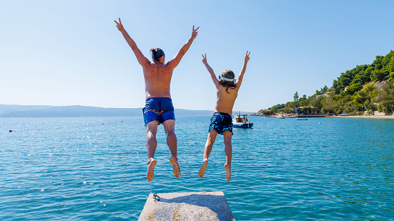 Father and young boy jumping in the air into sea- Vacation, summer holiday, travel destination concept- Happy family in vacation