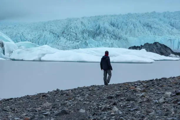 A lone male traveller, hiker, tourist at the edge of magnificent  Fjallsarlon Glacier Lagoon in Vatnajokull national park, surrounded by ice in scenic South Iceland