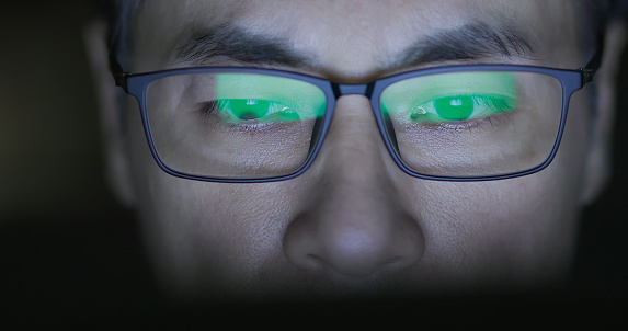close up eyes of asian senior businessman is working with computer at night and the commercial statements screen reflection on his glasses