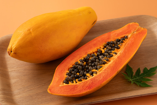 Fresh cut papaya fruit over orange table background for tropical gourmet design concept.