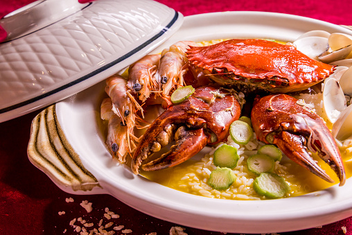 stewed mixed seafood platter crab, shell clam, tiger prawn in hot clay pot with rice and yellow chicken stock congee on red background restaurant food halal chinese banquet menu